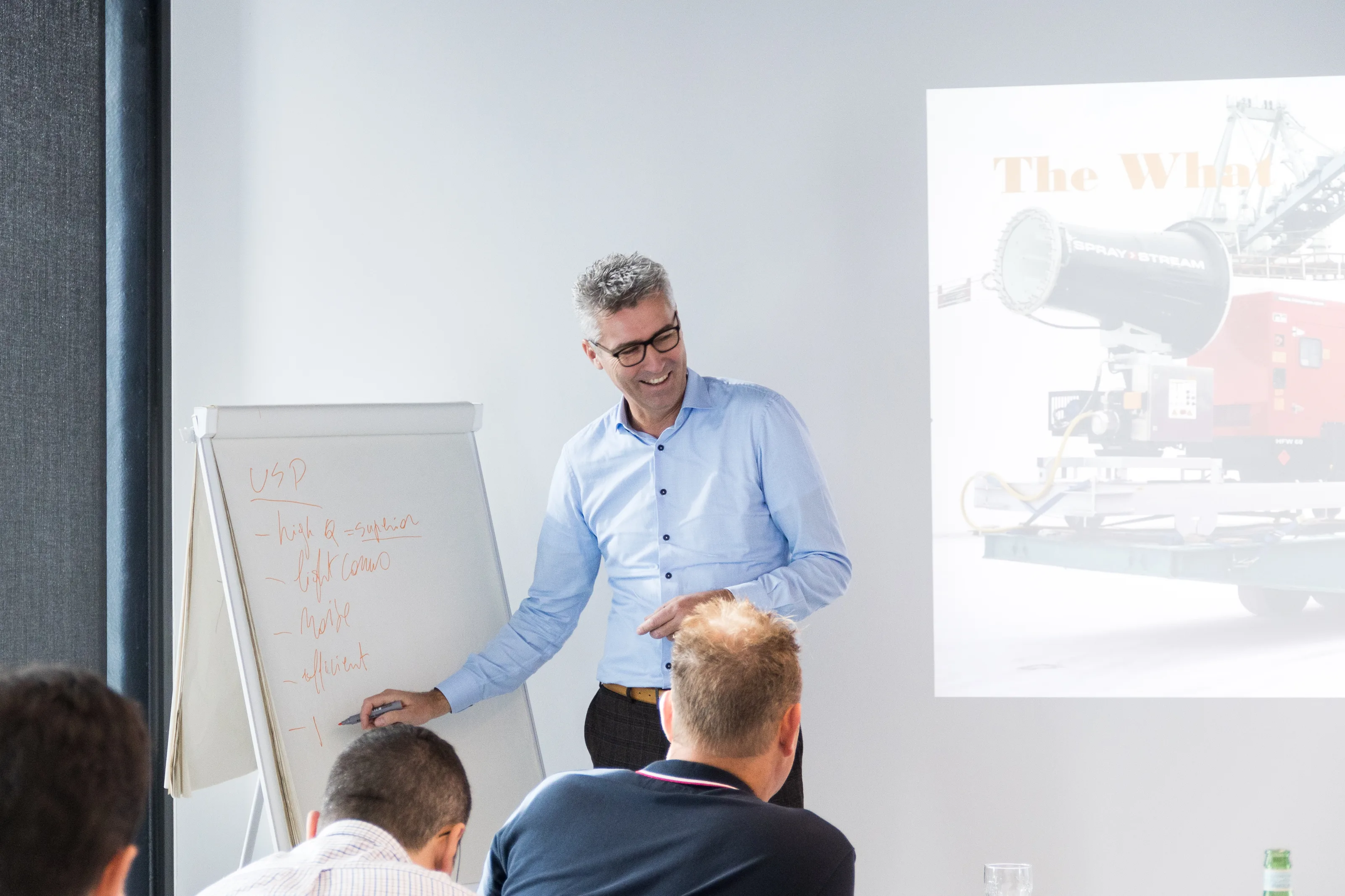 A coach in conversation with managers at a table, a flip chart beside the screen